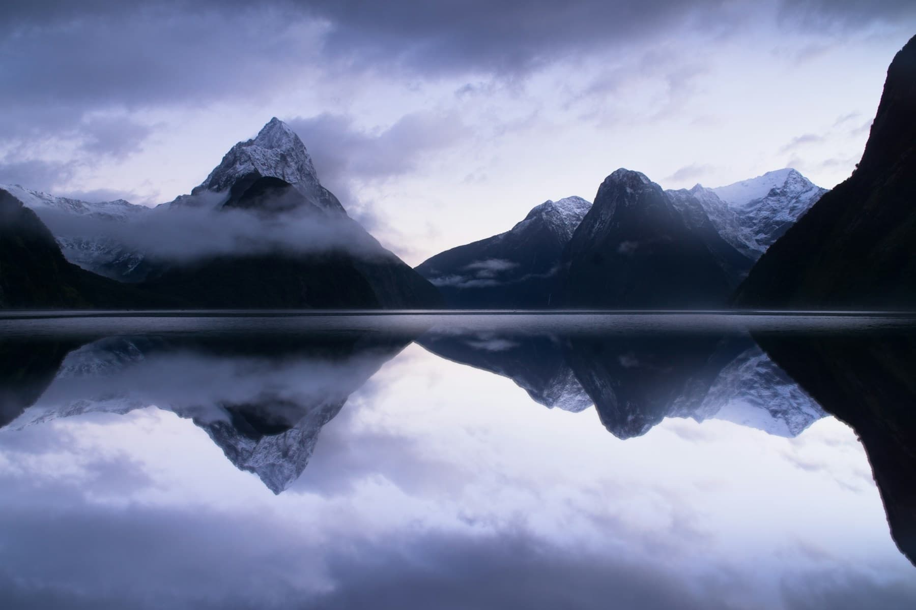 Mountain peaks reflected in the still water of Milford Sound