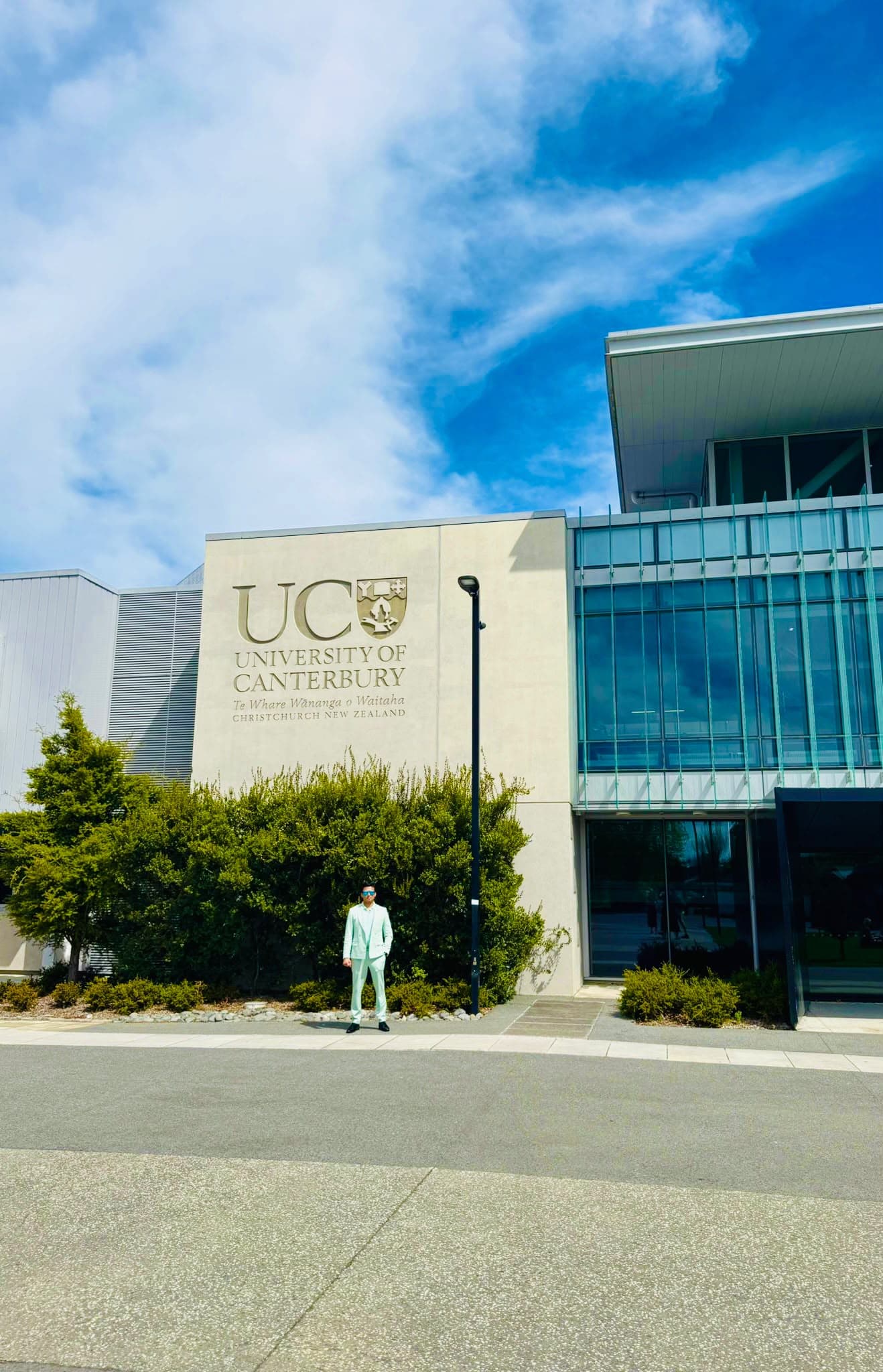 A visitor outside the University of Canterbury building beneath a blue sky